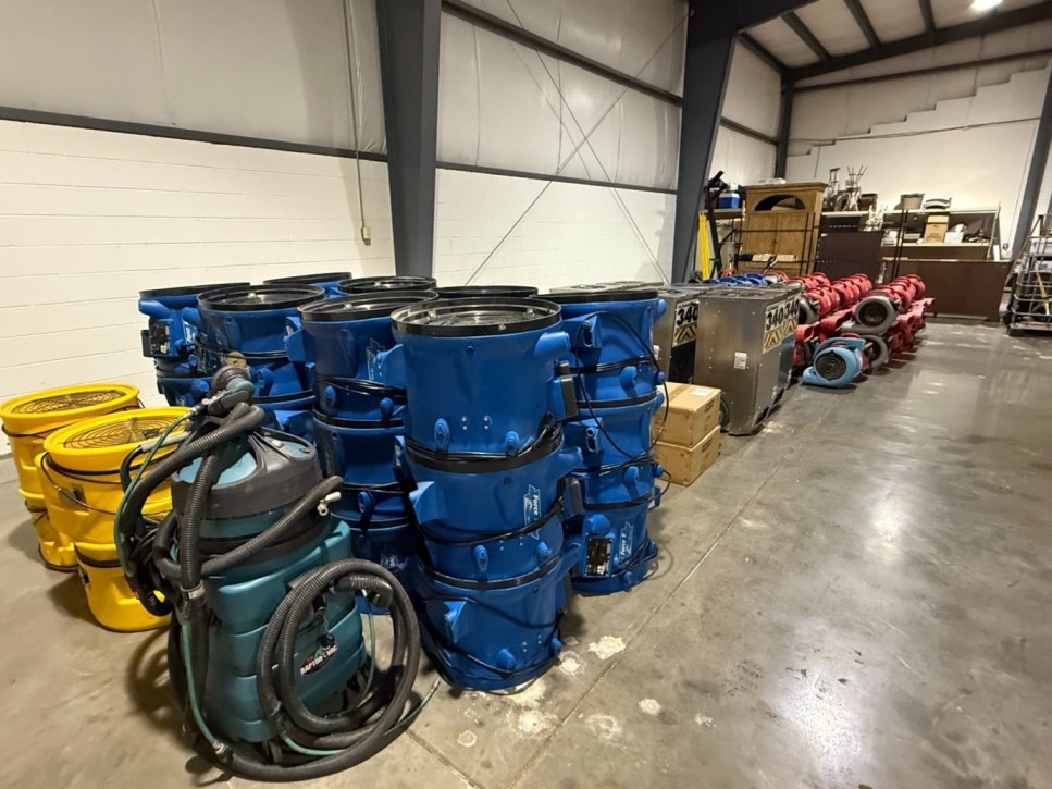 Rows of industrial air movers, HEPA vacuums, and commercial dehumidifiers inside a restoration warehouse ready for detailed mold remediation services.